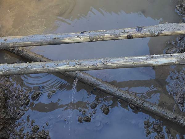 Three plumbing pipes with one leaking water.
