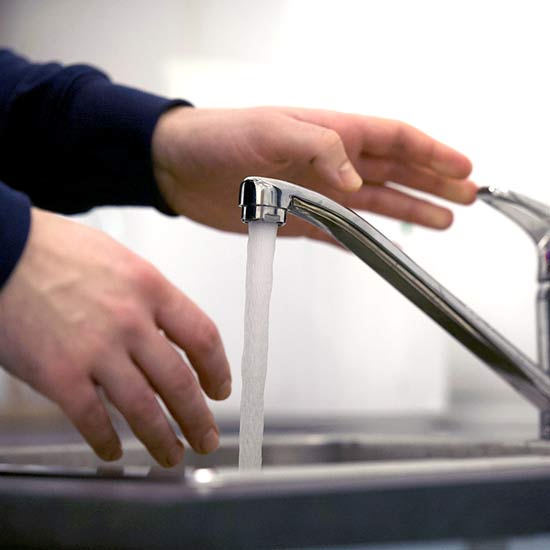 A person turning on running water from a faucet